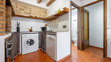 A compact kitchen with a washing machine, microwave, and wooden shelves.