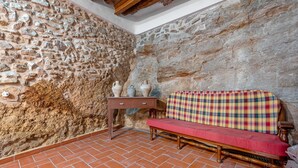 A stone-walled room with a red bench, a small table with vases, and terracotta-tiled flooring.