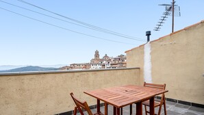 A wooden table and chairs on a balcony with a view of a historic building and mountains.