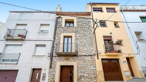 A multi-story building with a stone facade, a wooden door, and a balcony with potted plants.