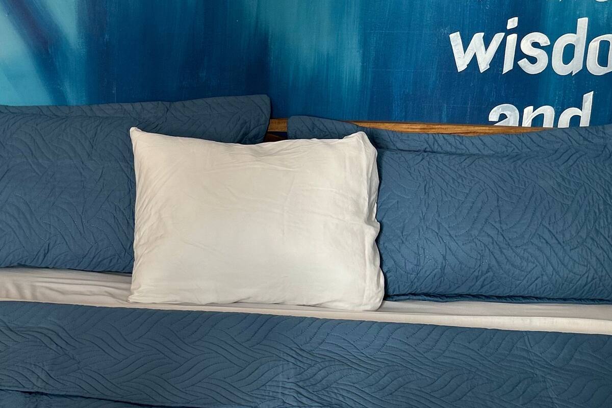 Un dormitorio con colcha azul, almohadas blancas y una mesita de noche con lámpara.