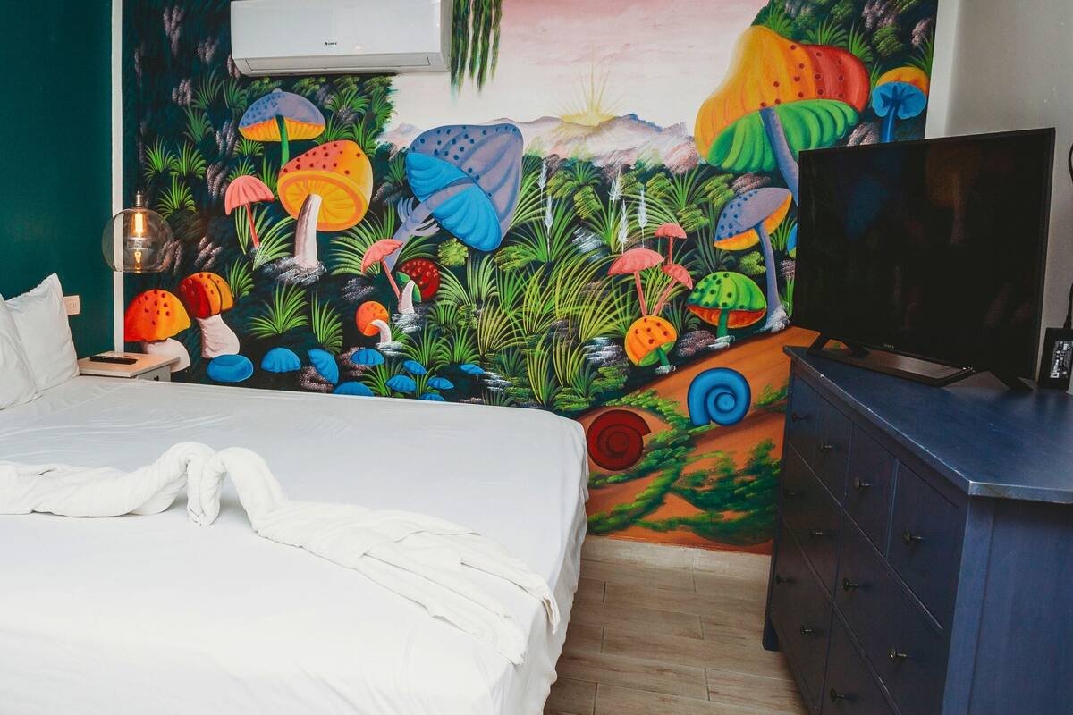 Un dormitorio con cama, televisor y un mural en la pared.