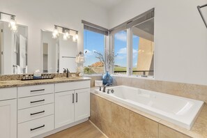 Ein modernes Badezimmer mit einer großen Badewanne, weißen Schränken und Blick auf eine Wüstenlandschaft durch das Fenster.