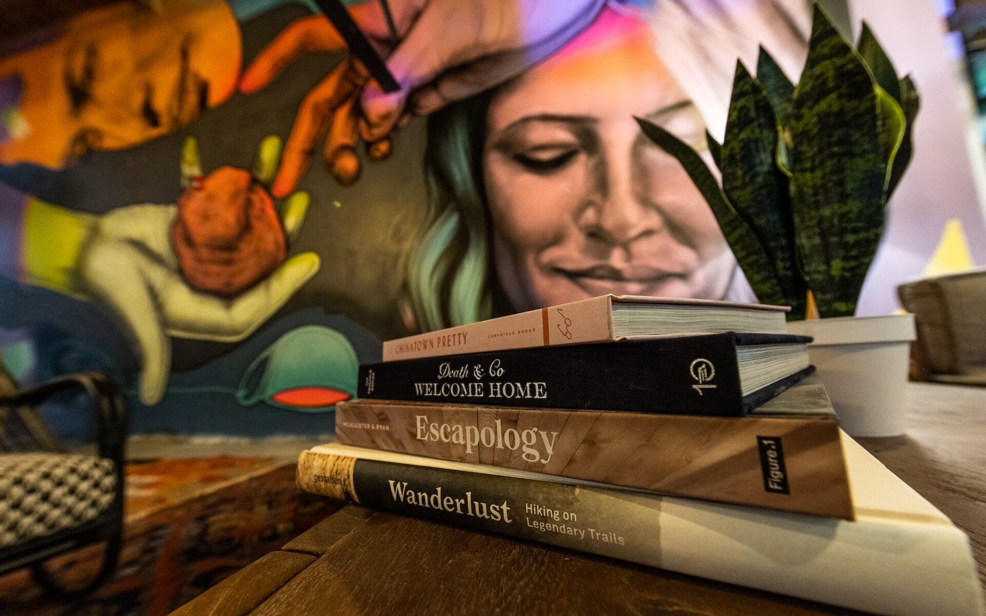 Een stapel boeken op een houten tafel, met een kleurrijke muurschildering op de achtergrond.