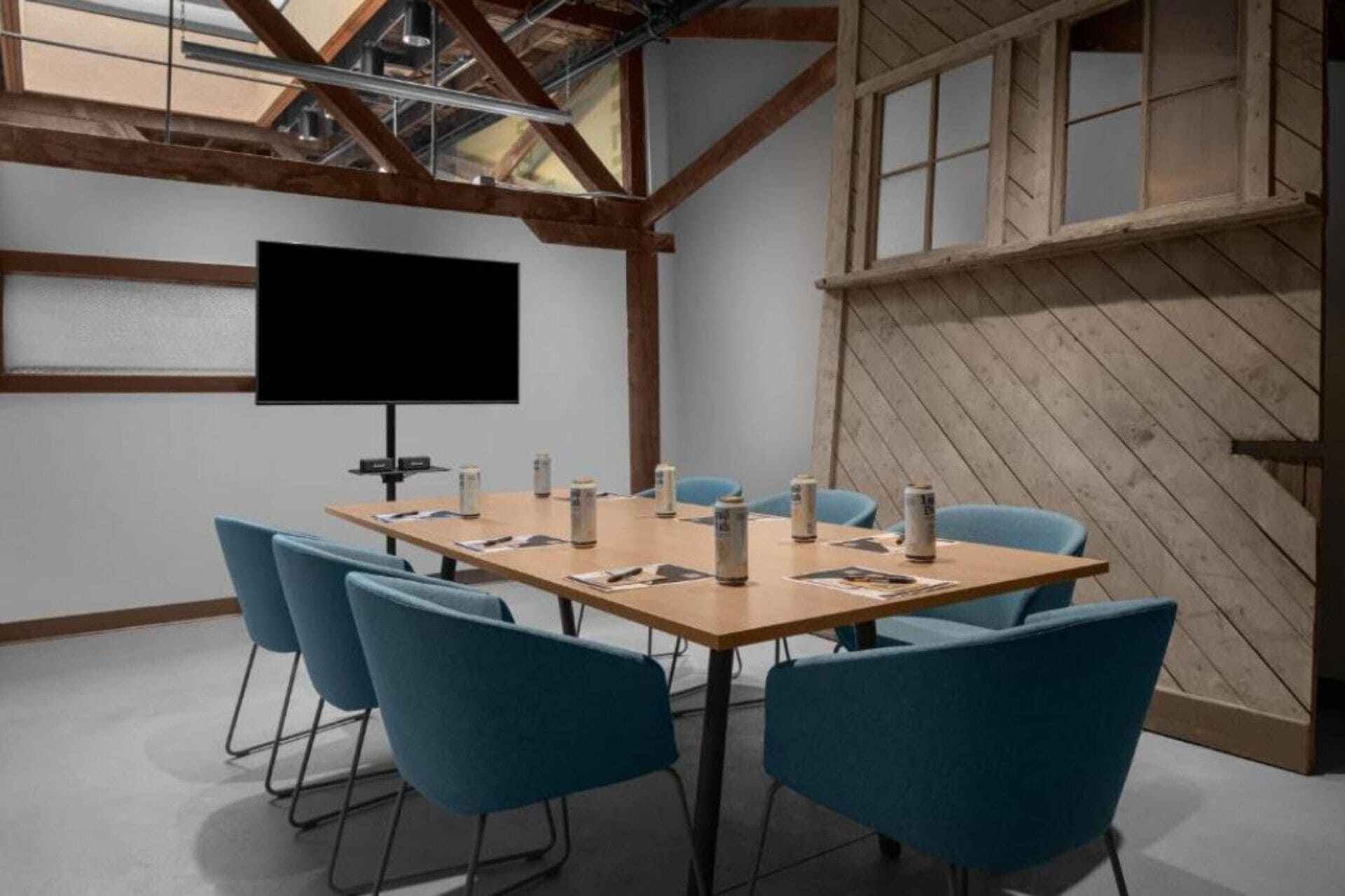 A conference room with a large table, blue chairs, a projector screen, and wooden beams.