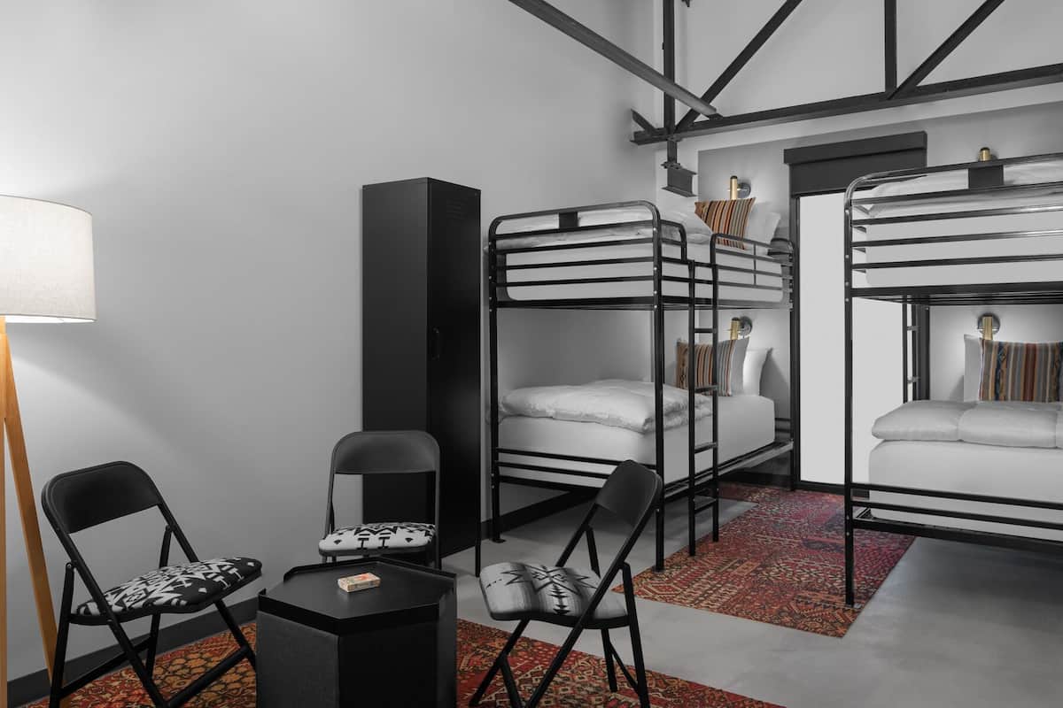 A compact room with bunk beds, a desk, two chairs, a lamp, and a small rug.