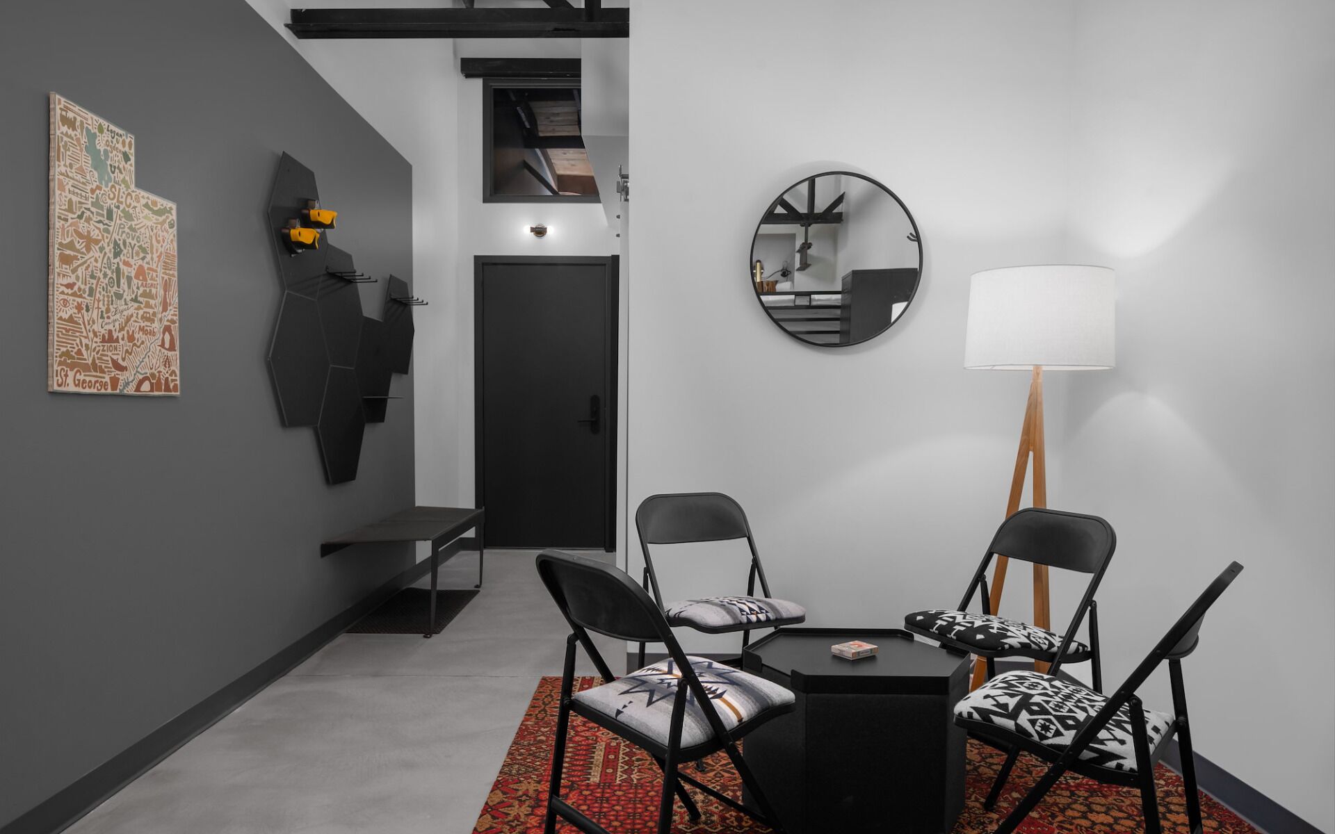 Une pièce moderne avec une table à manger noire, deux chaises, un tapis, un miroir et des œuvres d’art accrochées au mur.