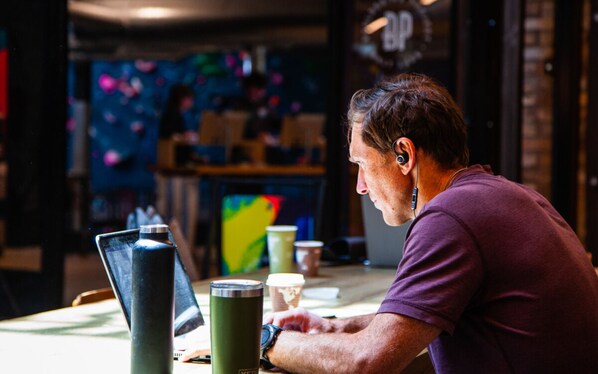 A person working at a table with a laptop, a green tumbler, and a cup. - Bposhtels SLC (Salt Lake City)