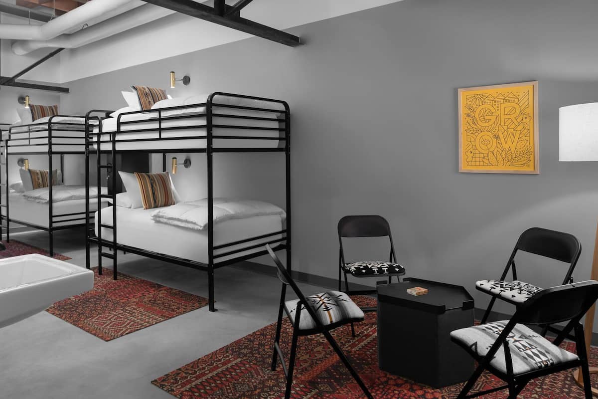 A bunk bed room with a red patterned rug, a black chair, a small black table, and a yellow artwork on the wall.