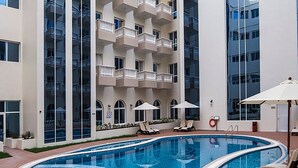 Una piscina interior moderna con sillas de descanso y sombrillas, rodeada por un edificio de varios pisos con balcones.