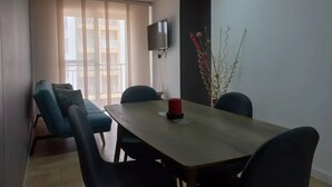 Un comedor moderno con una mesa larga, cuatro sillas, un televisor montado en la pared y una planta decorativa.