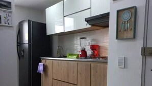 Una cocina con gabinetes de madera, un refrigerador negro, una cafetera roja y una licuadora en la encimera.
