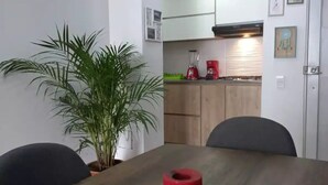Un comedor con una mesa de madera, sillas, una planta en maceta y una cocina al fondo.