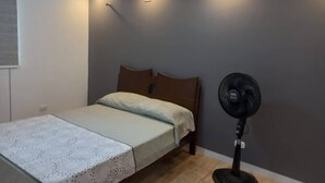 Un dormitorio con cama, ventilador de pie e iluminación empotrada en el techo.