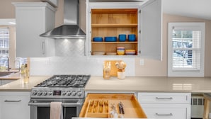 A modern kitchen with a gas stove, a stainless steel range hood, and a wooden cabinet with blue and yellow dishes. - The ARLO - Walk to Brewery and Restaurants (Milford)