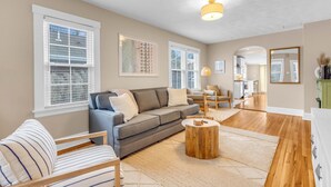 A spacious living room with a grey sofa, striped armchair, and a round wooden coffee table. - The ARLO - Walk to Brewery and Restaurants (Milford)