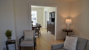 A living room with a grey sofa, a wooden dining table with chairs, a cabinet, and a lamp.
