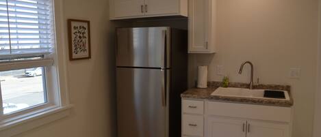 A kitchen with white cabinets, a stainless steel refrigerator, a granite countertop, and a window with blinds.