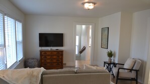 A living room with a sofa, a television, a wooden dresser, a chair, and a small table with a plant.