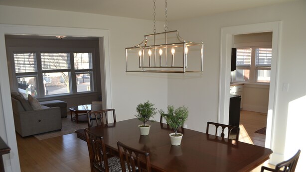 A dining area with a wooden table, six chairs, and two potted plants.