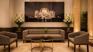 A modern lounge area with a sofa, two armchairs, and a coffee table, featuring a large framed artwork of a building. - Hotel Bellas Artes  (Mexico City)