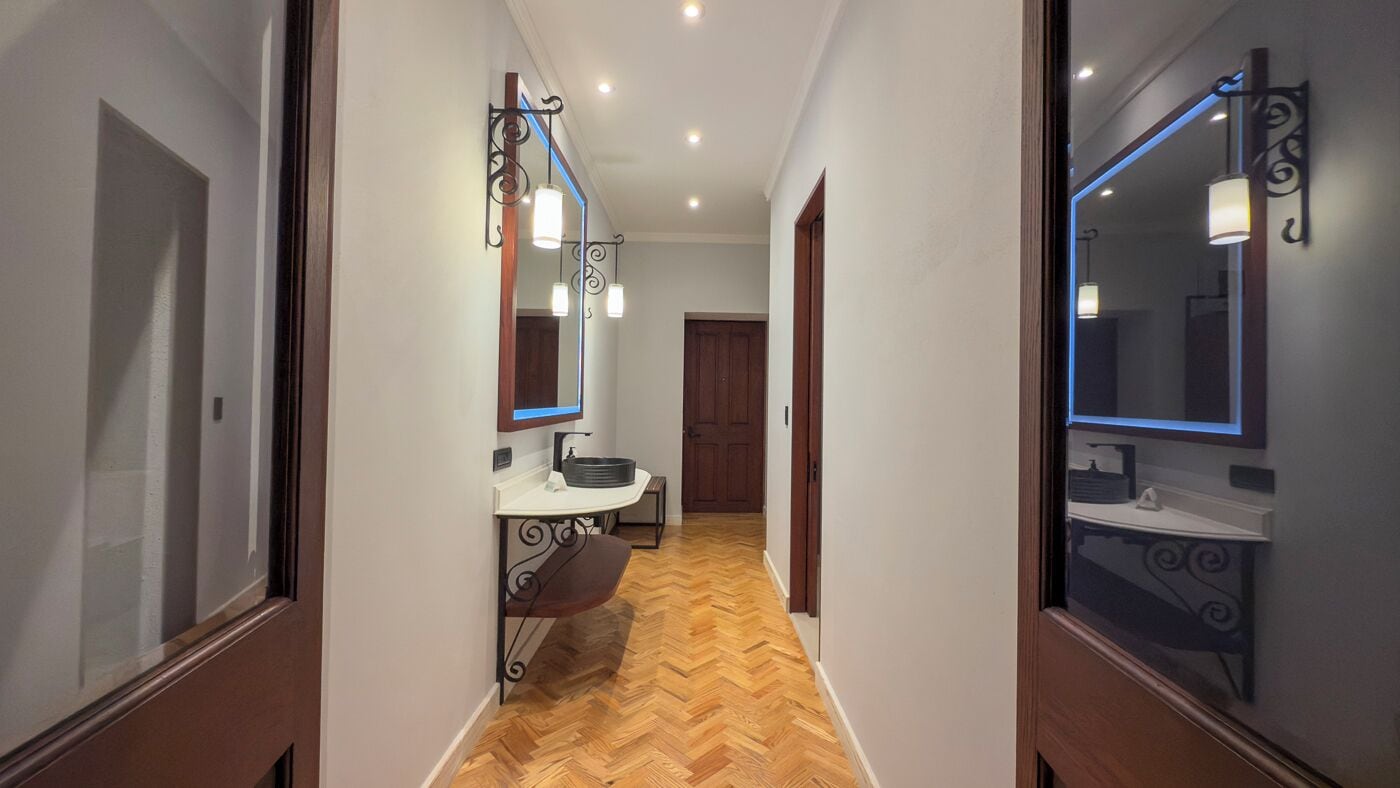A hallway with a wooden floor, a white sink, and a mirror with a light fixture.