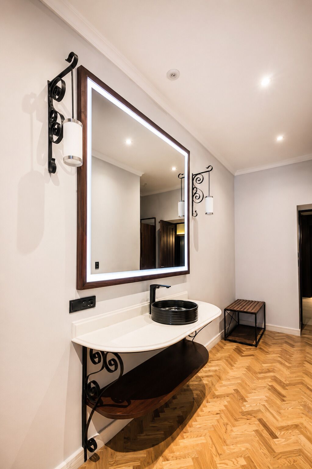 A modern bathroom with a large mirror, a white sink, and a wooden bench.