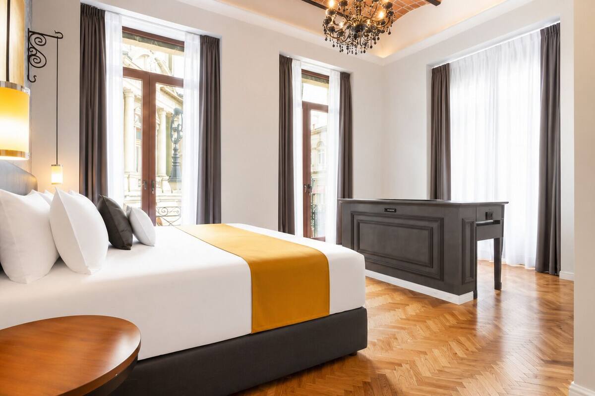 A hotel room with a bed, a desk, a chair, and a chandelier.