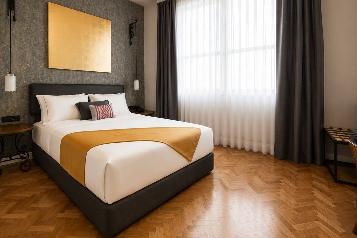 A hotel room with a large bed, a desk, a chair, a wall-mounted lamp, and a window with curtains.