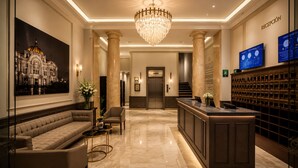 A lobby with a reception desk, a sofa, a chandelier, a large painting, and a wall-mounted clock. - Hotel Bellas Artes  (Mexico City)