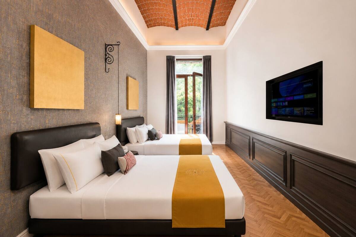 A hotel room with two beds, a TV, and a view of greenery outside.