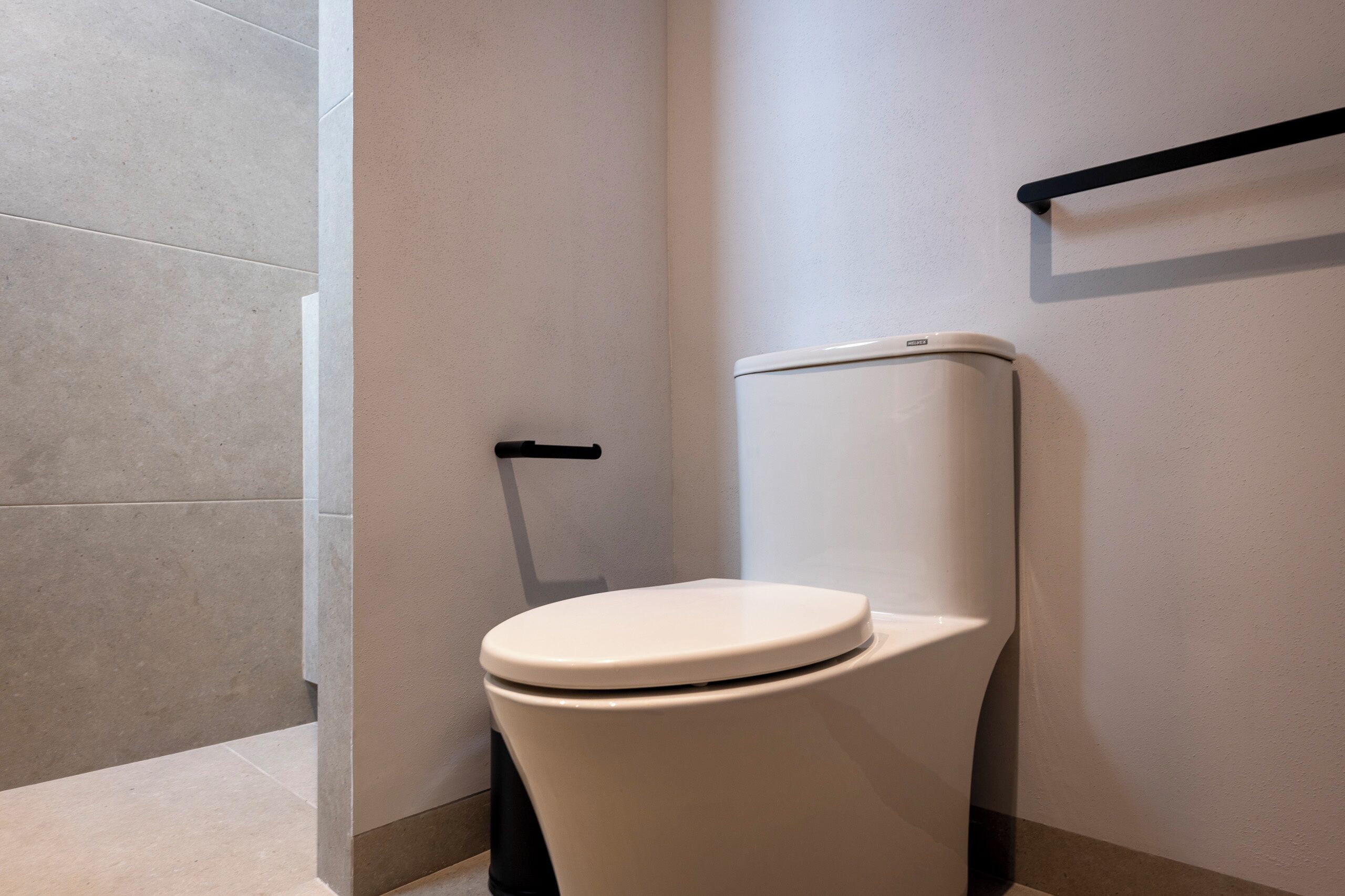 A modern bathroom with a white toilet, a black grab bar, and a tiled floor.