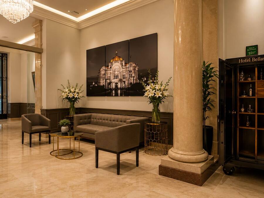 A lobby with a sofa, chairs, a round table, a large column, and a display cabinet with bottles.