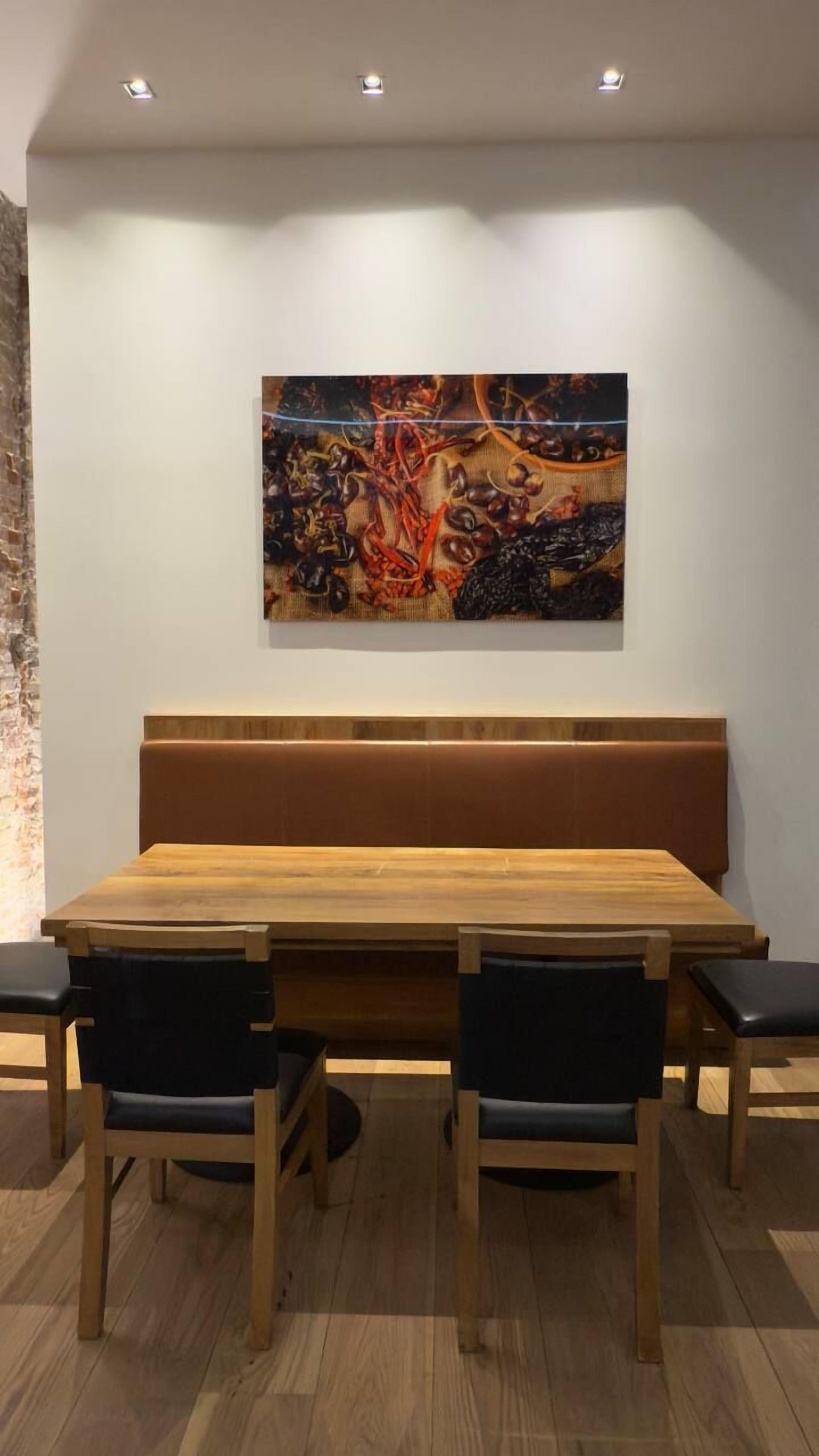 Un comedor con una mesa de madera y cuatro sillas, un banco y un cuadro colgado en la pared.