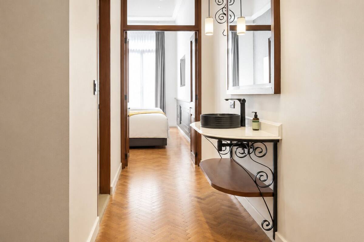 A hallway with a wooden floor leading to a room with a bed and a window.