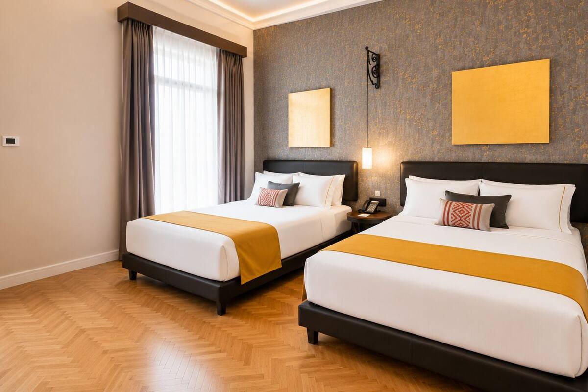 A hotel room with two beds, a wooden floor, a wall-mounted phone, and a window with curtains.