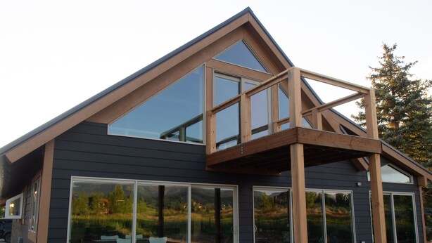 Une maison moderne dotée de grandes fenêtres, d’une terrasse en bois et d’un escalier menant à un étage supérieur.