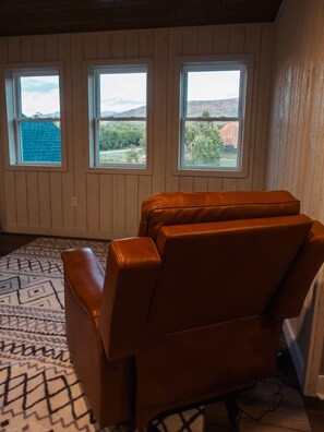 A room with a brown leather chair, three windows, and a patterned rug. - Grand Lodging Company (Driggs)