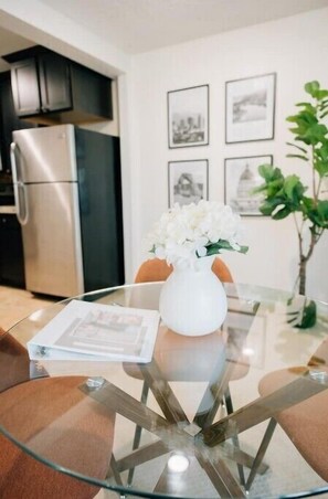 Una cocina moderna con electrodomésticos de acero inoxidable, una mesa de comedor de vidrio con un florero blanco y cuadros en la pared.