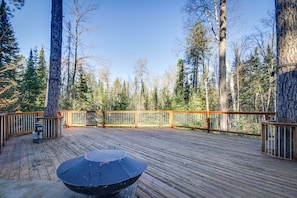 A wooden deck with a barbecue grill, surrounded by tall trees and a clear sky.