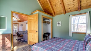 A bedroom with a plaid bedspread, wooden ceiling beams, a desk, and a chair.
