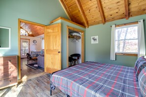A bedroom with a plaid bedspread, wooden ceiling beams, a desk, and a chair.