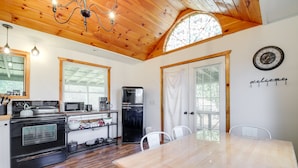 A kitchen with a wooden ceiling, a stove, microwave, refrigerator, and a dining table with chairs.