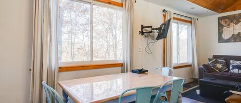 Habitació acollidora amb sostre de fusta, taula de dinar amb cadires, sofà i televisió penjada.