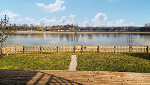 A wooden deck with a clear view of a calm lake, a wooden fence, and a pathway leading to the water.