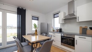 A modern kitchen with a dining area, featuring a large window, a built-in oven, and a view of a body of water.