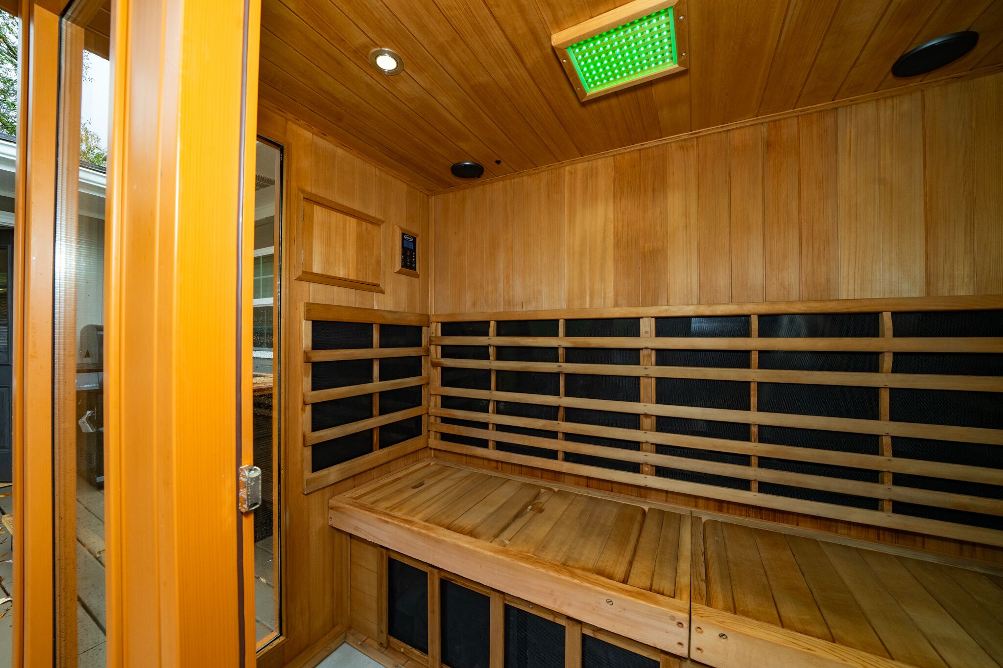 A sauna with wooden walls and benches, a control panel, and a green light on the ceiling.