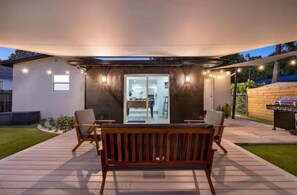 Un espace extérieur aménagé en patio, avec un banc en bois, deux chaises et un barbecue.