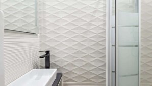 A modern bathroom with a geometric patterned wall, a white sink, and a glass shower enclosure. - Appart T2 Cosy et Chaleureux au coeur du 11eme (Paris)