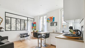 A modern kitchen with a central island, bar stools, and a dining area with a table and chairs. - Appart T2 Cosy et Chaleureux au coeur du 11eme (Paris)